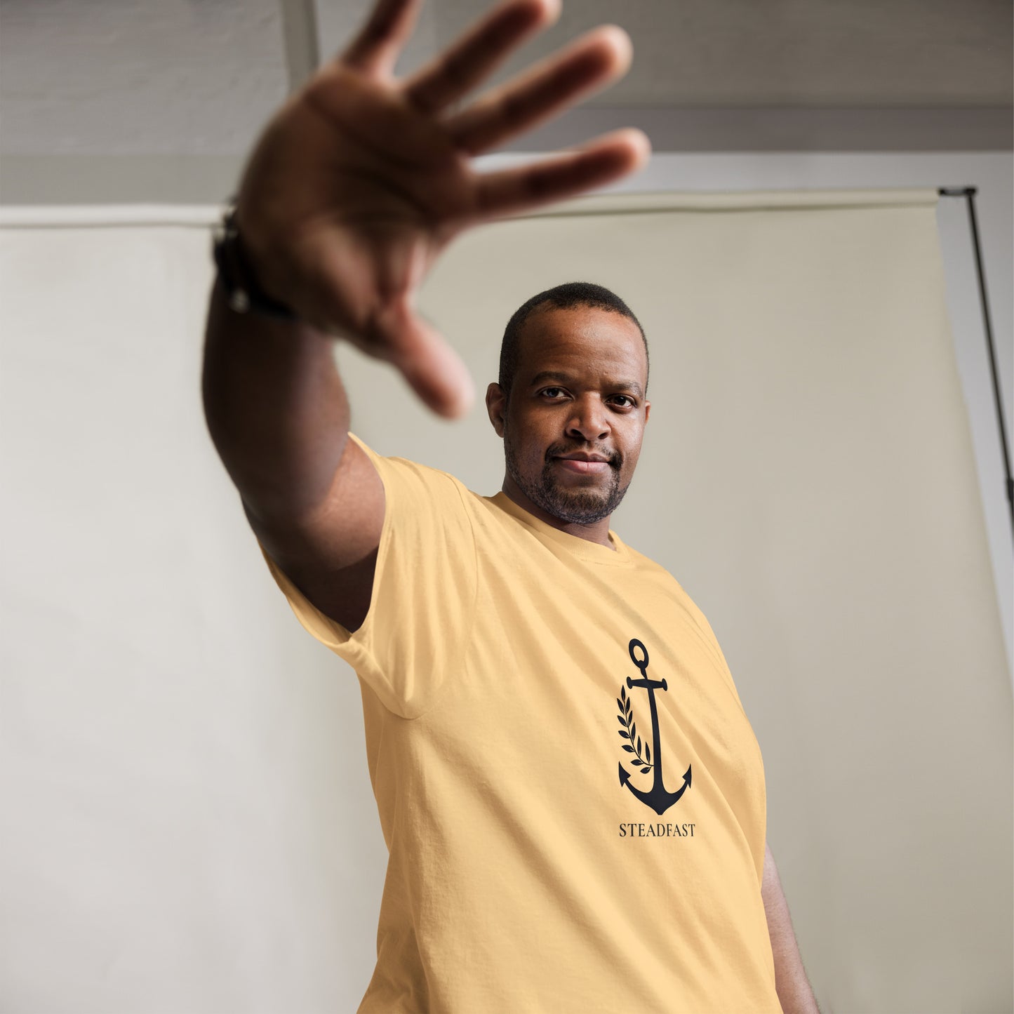 Man model wearing yellow Christian t-shirt withchor design. Anchor and steadfast text visible casual pose