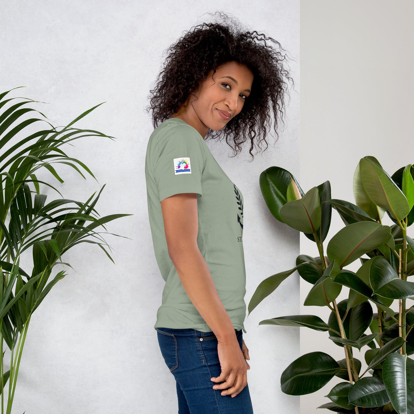 Woman modeling green Christian anchor shirt for men and women side view with jeans and plants