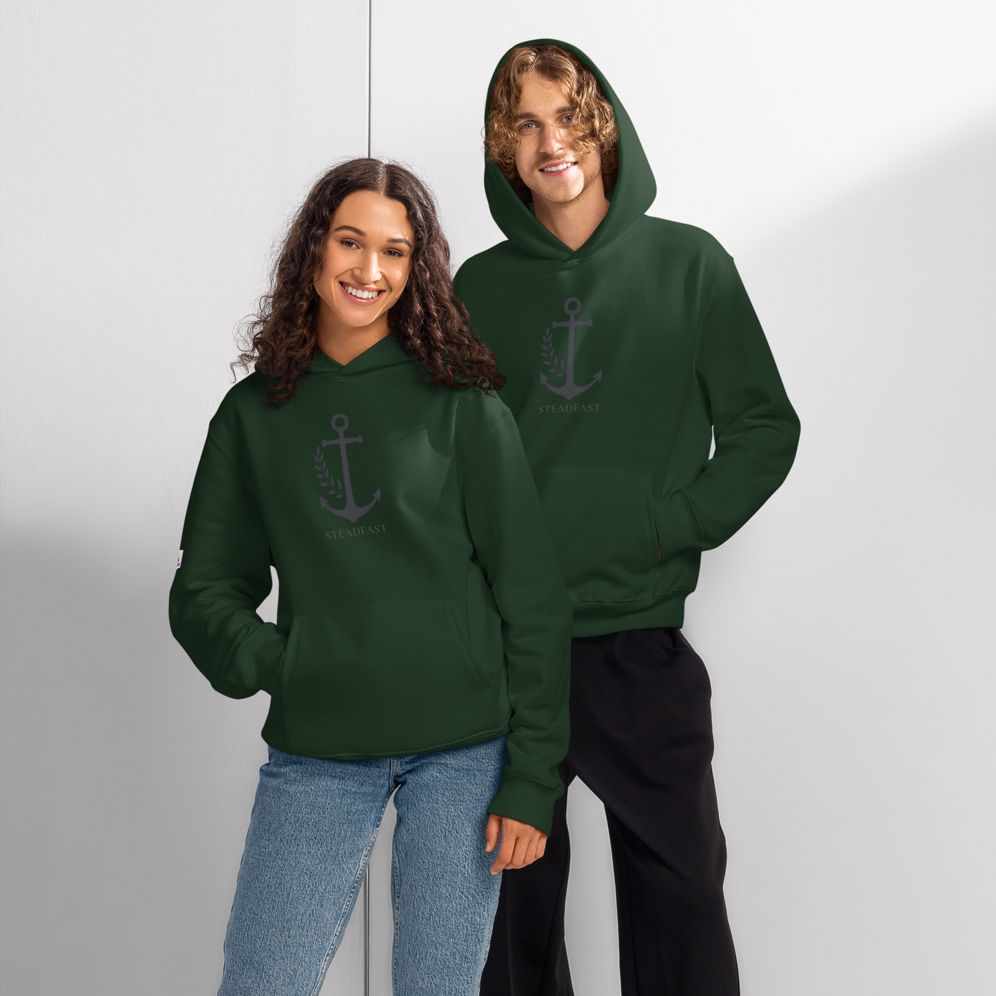 Two smiling models wearing dark green oversized religious hoodie for adults with anchor graphic Spirit Wear logo
