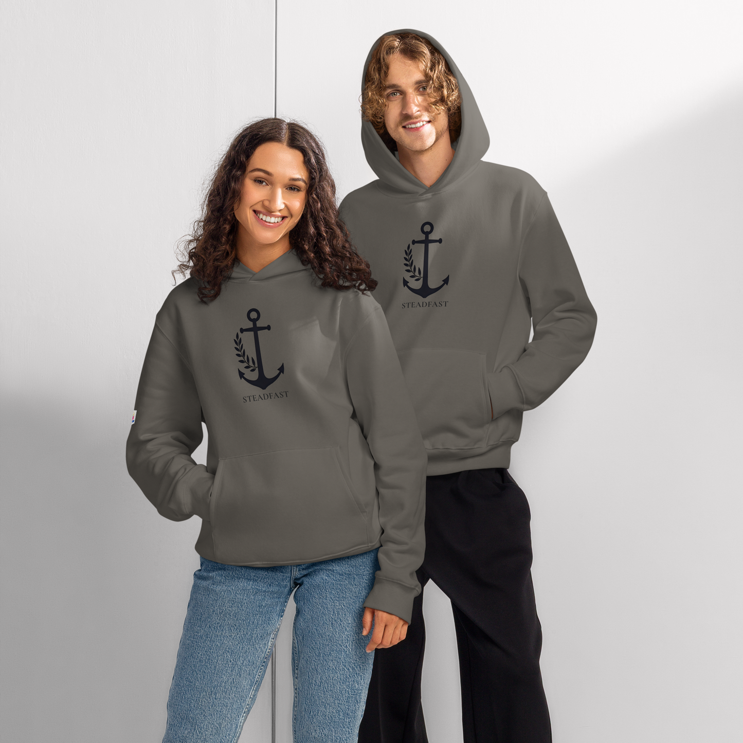 Two smiling adults wearing charcoal gray oversized religious hoodie for adults with anchor laurel emblem