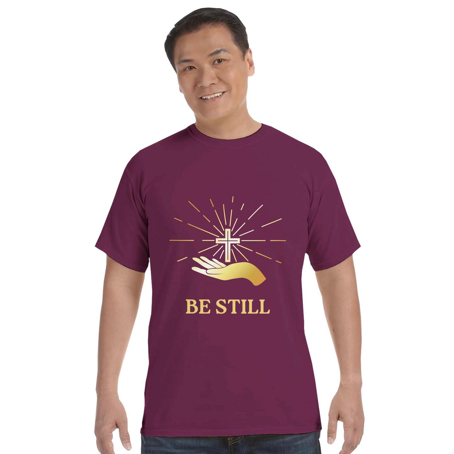 Christian graphic t-shirt in maroon featuring a gold cross and hand design with the phrase Be Still