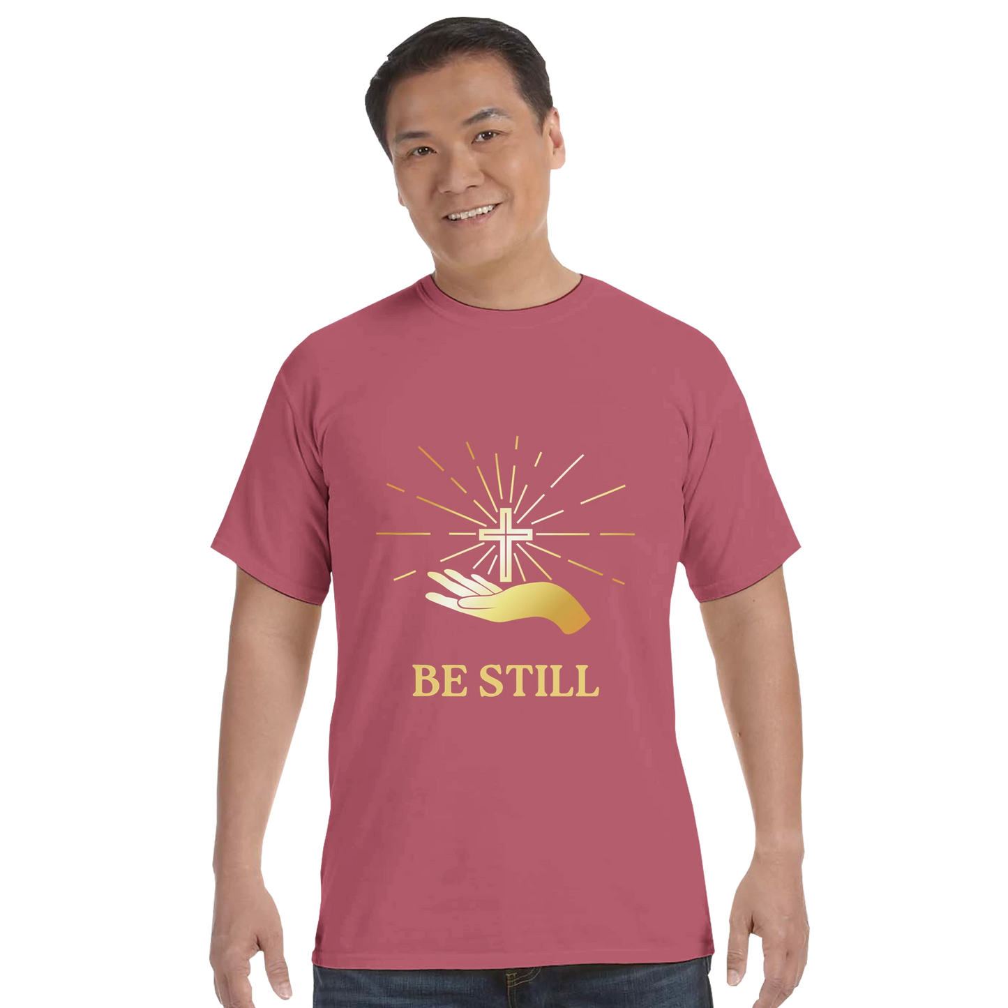 Christian graphic t-shirt featuring a cross and the phrase Be Still in gold on a maroon background