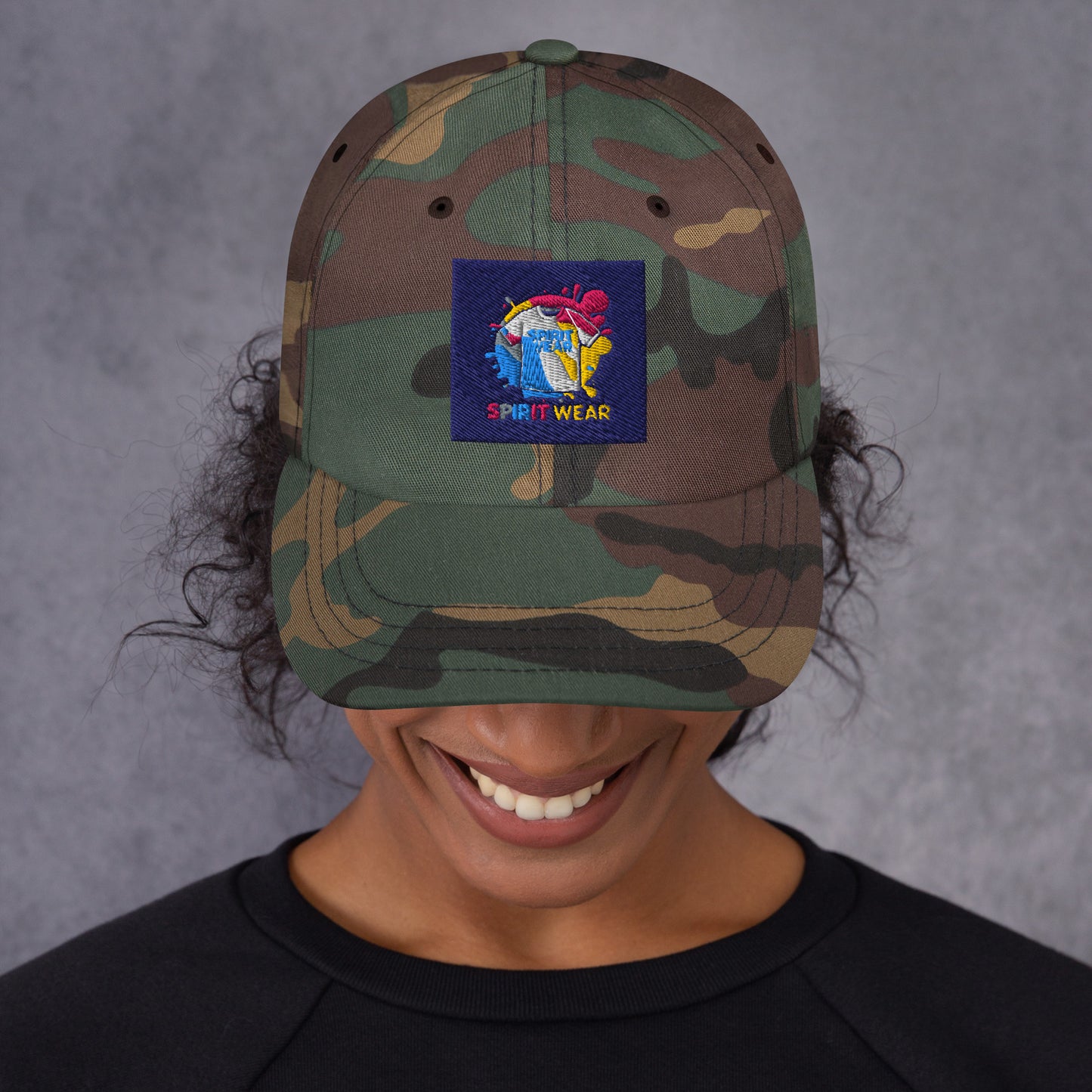 Spirit Wear camo Christian ball cap with colorful logo patch worn by a smiling person