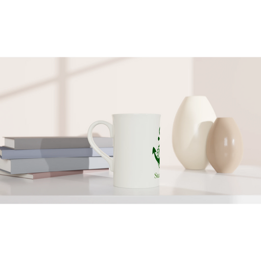 Spirit Wear Peace Pack Collection slim mug white ceramic with green logo on desk beside stacked books and decorative vases