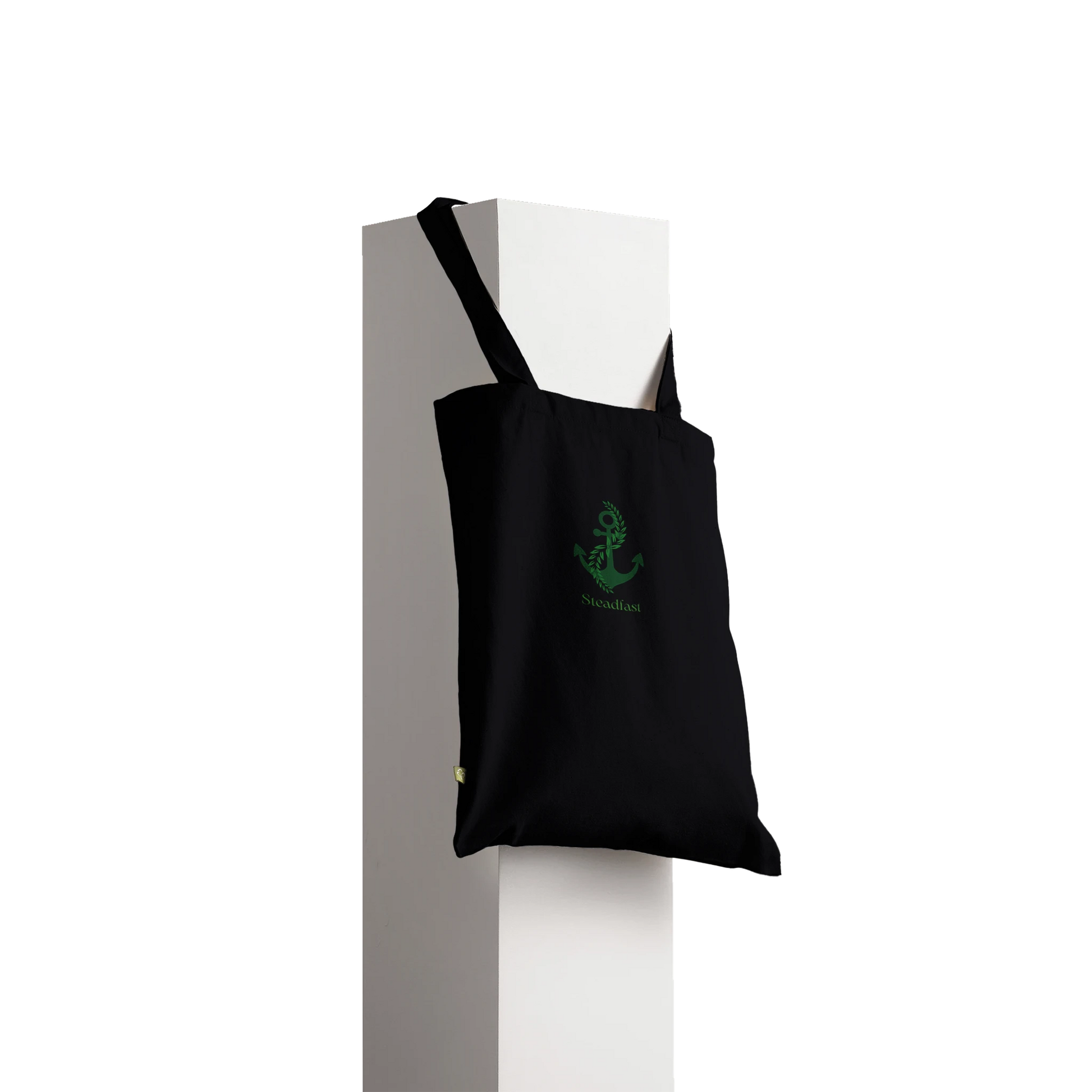 Black canvas Spirit Wear peace pack collection tote with green anchor logo hanging from white pedestal